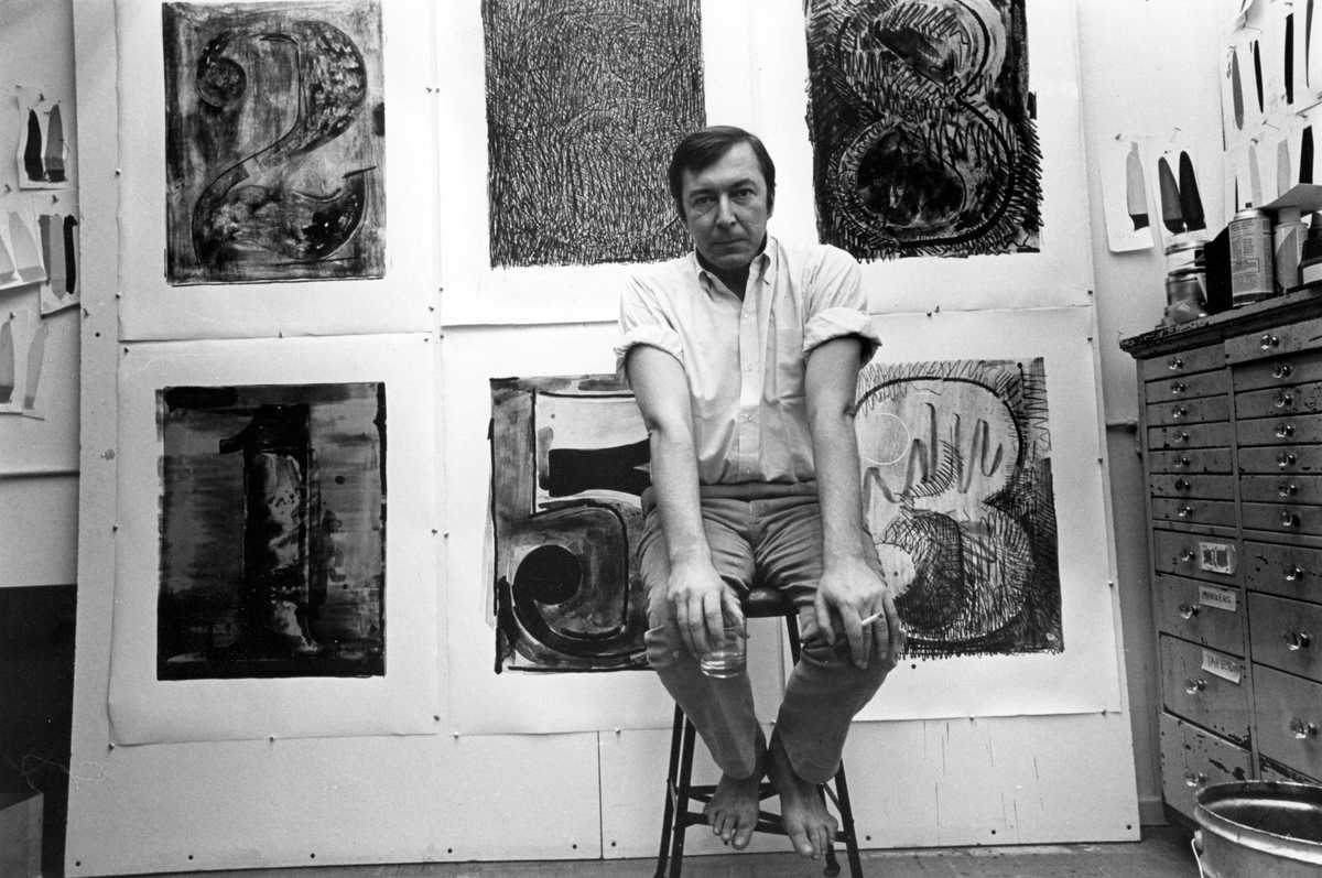 Jasper Johns sits on a stool in front of his Black Numeral series of prints